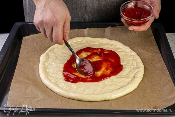 Застелите противень бумагой, выложите тесто, равномерно смажьте кетчупом.