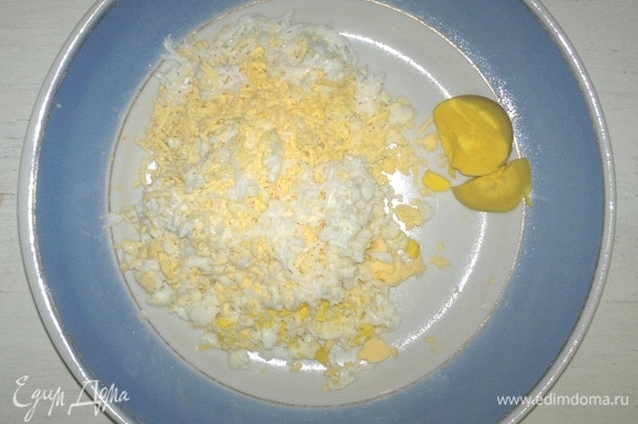 Яйца сварить вкрутую, остудить в холодной воде. Вареные яйца почистить. Немного желтка отложить для украшения. Яйца натереть на мелкой терке.