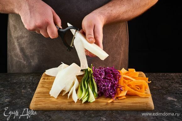 Приготовьте гарнир. С помощью овощечистки нарежьте слайсами цукини, морковь, дайкон, краснокочанную капусту.