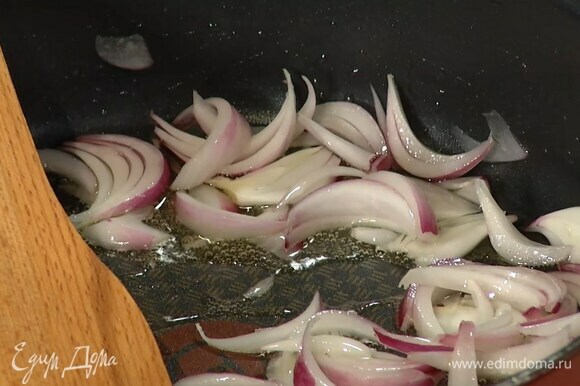 Красный лук почистить и нарезать тонкими дольками, затем разогреть в сковороде оливковое масло и обжарить лук до золотистого цвета.