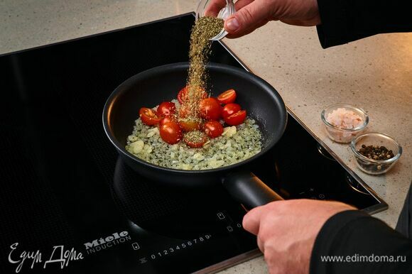На индукционную панель конфорок Miele поставьте сковороду, добавьте оливковое и сливочное масло, обжарьте лук и чеснок до мягкости. Добавьте черри и орегано. Посолите, поперчите. Протушите 5 минут.