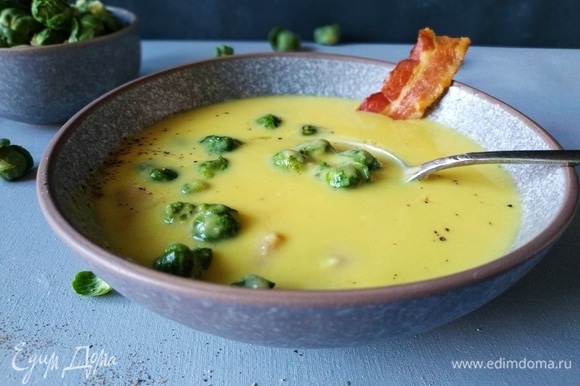 Горячий крем-суп разлейте по тарелкам. Добавьте в каждую тарелку кусочек бекона и брюссельскую капусту, поперчите и подавайте к столу. Приятного аппетита.