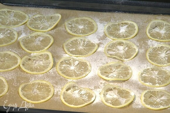 Два лимона для украшения нарезать очень тонкими кружками и выложить на противень, выстеленный бумагой для выпечки, через сито посыпать сахарной пудрой и запекать в разогретой духовке около часа.