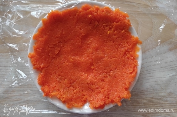 Блюдце застелить кусочком пищевой пленки и выложить ложку моркови, разровнять по кругу, чтобы получилась лепешка.