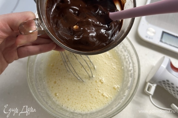 Отдельно в миске взбить яйца с сахаром в пышную белую пену. Добавить остывший шоколад с маслом и еще раз перемешать.