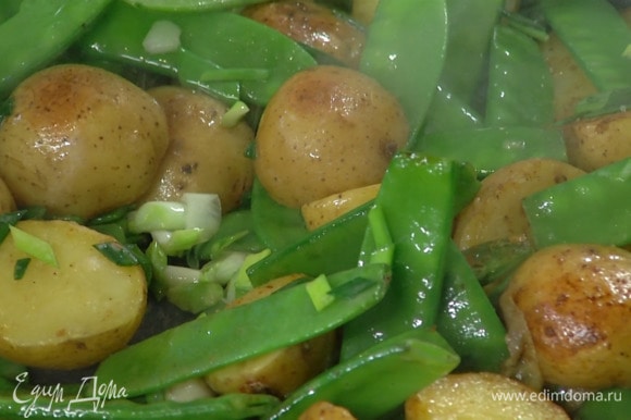 Зеленый лук нарезать наискосок и добавить к картофелю вместе с горошком, посолить и обжаривать еще буквально минуту.
