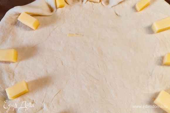 Тесто раскатать в круг диаметром 30 см. Сыр нарезать на 12 кусочков и разложить по кругу, защипать края.
