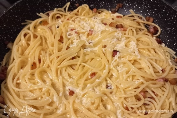 После готовности бекона отправляем в сковороду спагетти, перемешиваем. Через 1–2 минуты вливаем смесь желтка со сливками и сыром. На среднем огне слегка перемешиваем блюдо. Сверху поливаем 1 ст. л. оливкового масла. Соус в это время доходит до готовности от тепла сваренной пасты, поэтому готовим ингредиенты последовательно, а также не даем им остыть. Важно не передержать блюдо на данном этапе, иначе яично-сливочно-сырная масса свернется и блюдо будет сухим.