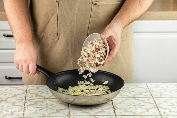 В это время мелко нарежьте лук и шампиньоны. Выложите в сковороду лук и слегка обжарьте, следом добавьте грибы, оставьте смесь на среднем огне под крышкой на 5 минут.