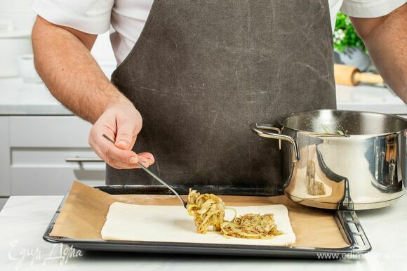 Тонко раскатайте пласт слоеного теста, выложите на него луковую начинку и заверните края. Добавьте оливки и отправьте пирог в духовку, разогретую до 180°С, на 20–25 минут.